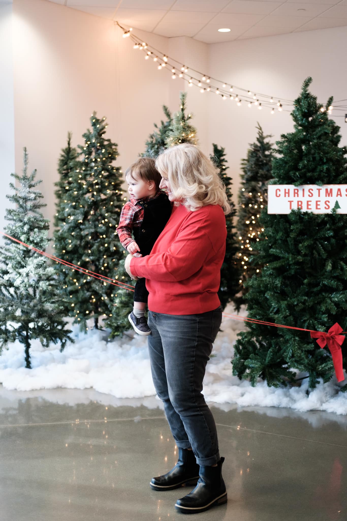 Christmas Adult holding child in front of Christmas trees.